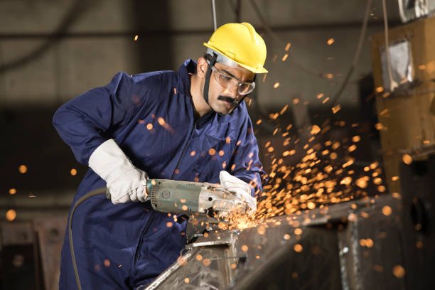 Mechanic using circular saw grinder tool with protective work wear at factory